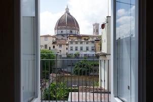 A view from a balcony with a metal railing, overlooking a cityscape with historic buildings and a prominent dome structure.
