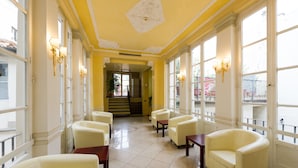 Rebedor d'hotel amb una decoració de groc i blanc, que destaca una escala central, zona d'estar amb cadires i grans finestres.
