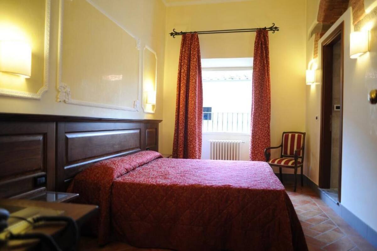 A hotel room with a large bed, a wooden nightstand, a chair, and a window with curtains.