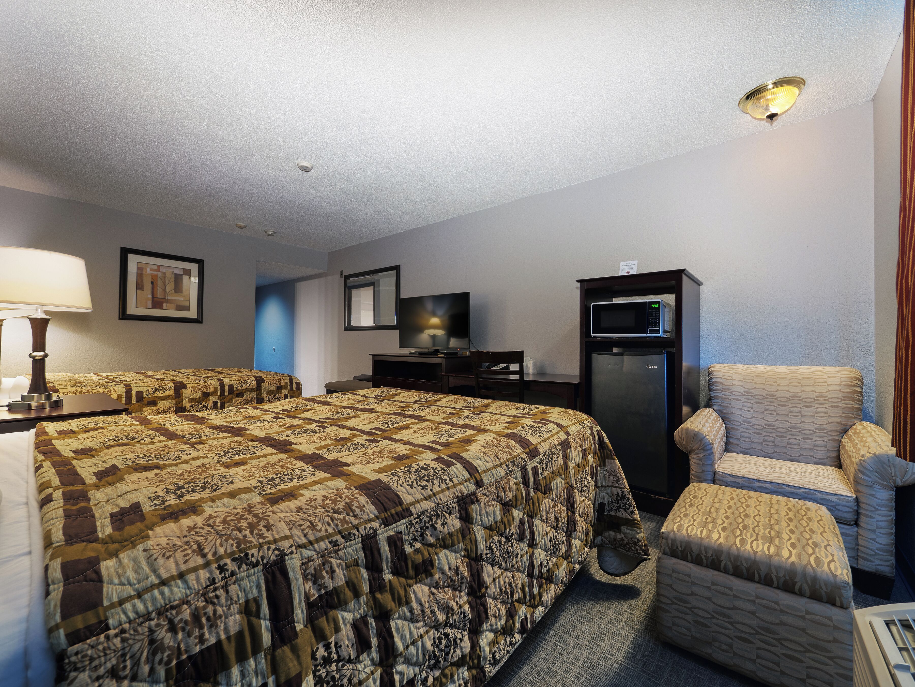 A hotel room with a large bed, a chair, a desk, a television, and a refrigerator.