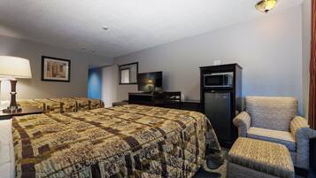 A hotel room with a large bed, a chair, a desk, a television, and a refrigerator.