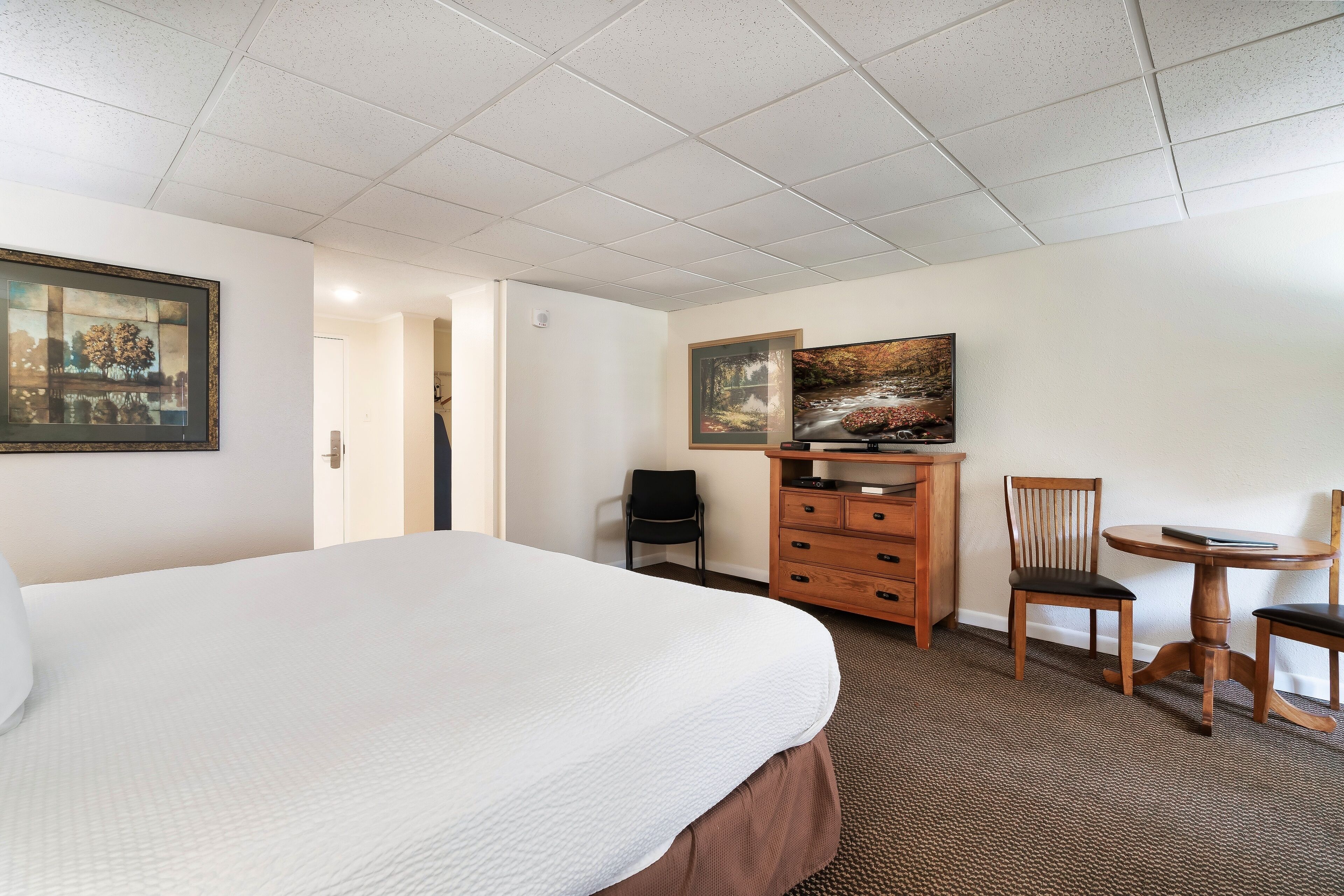 Ein Hotelzimmer mit einem großen Bett, einer Holzkommode, zwei Stühlen und zwei Bildern an der Wand.