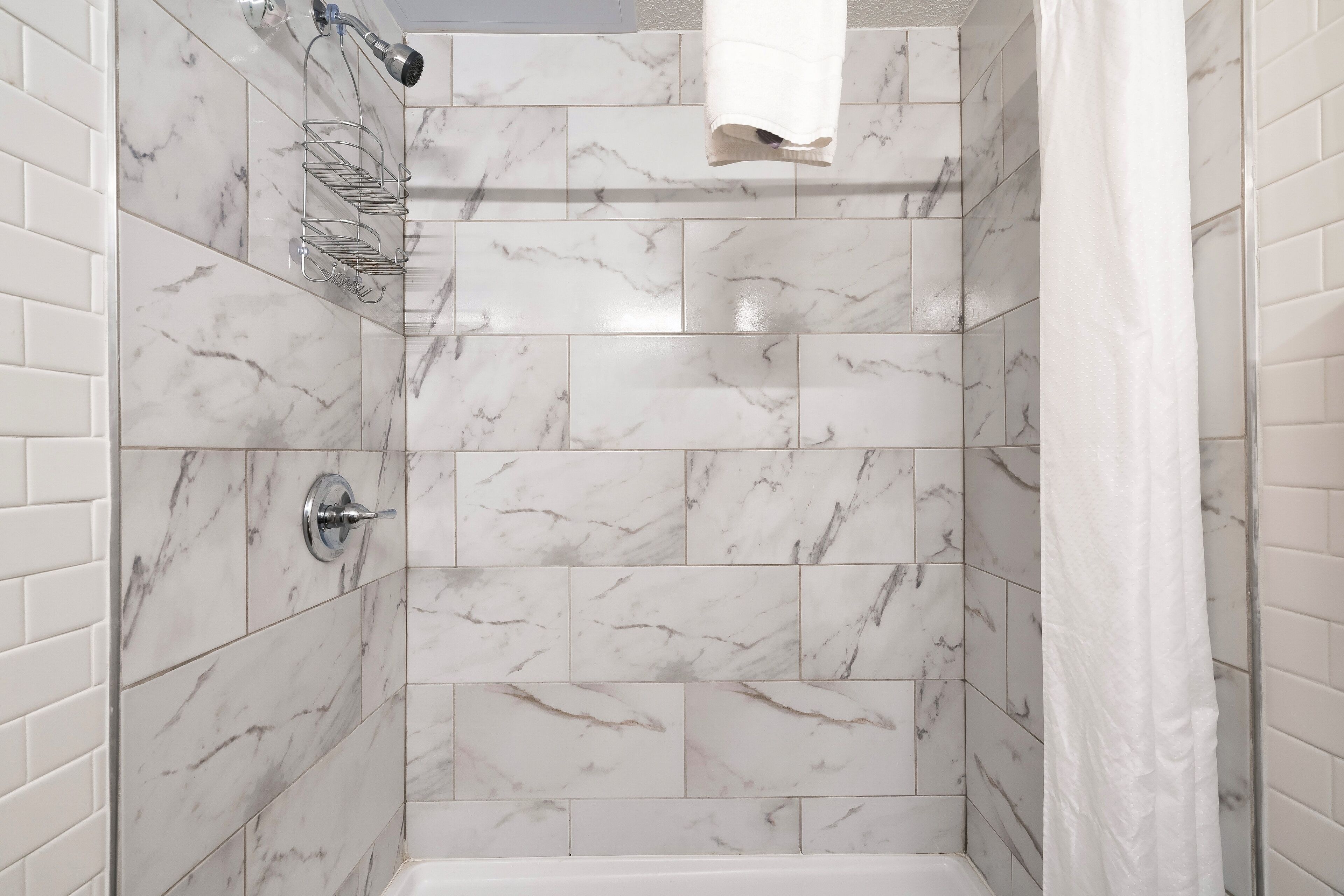 A bathroom with white marble tiles, a shower, and a towel rack.