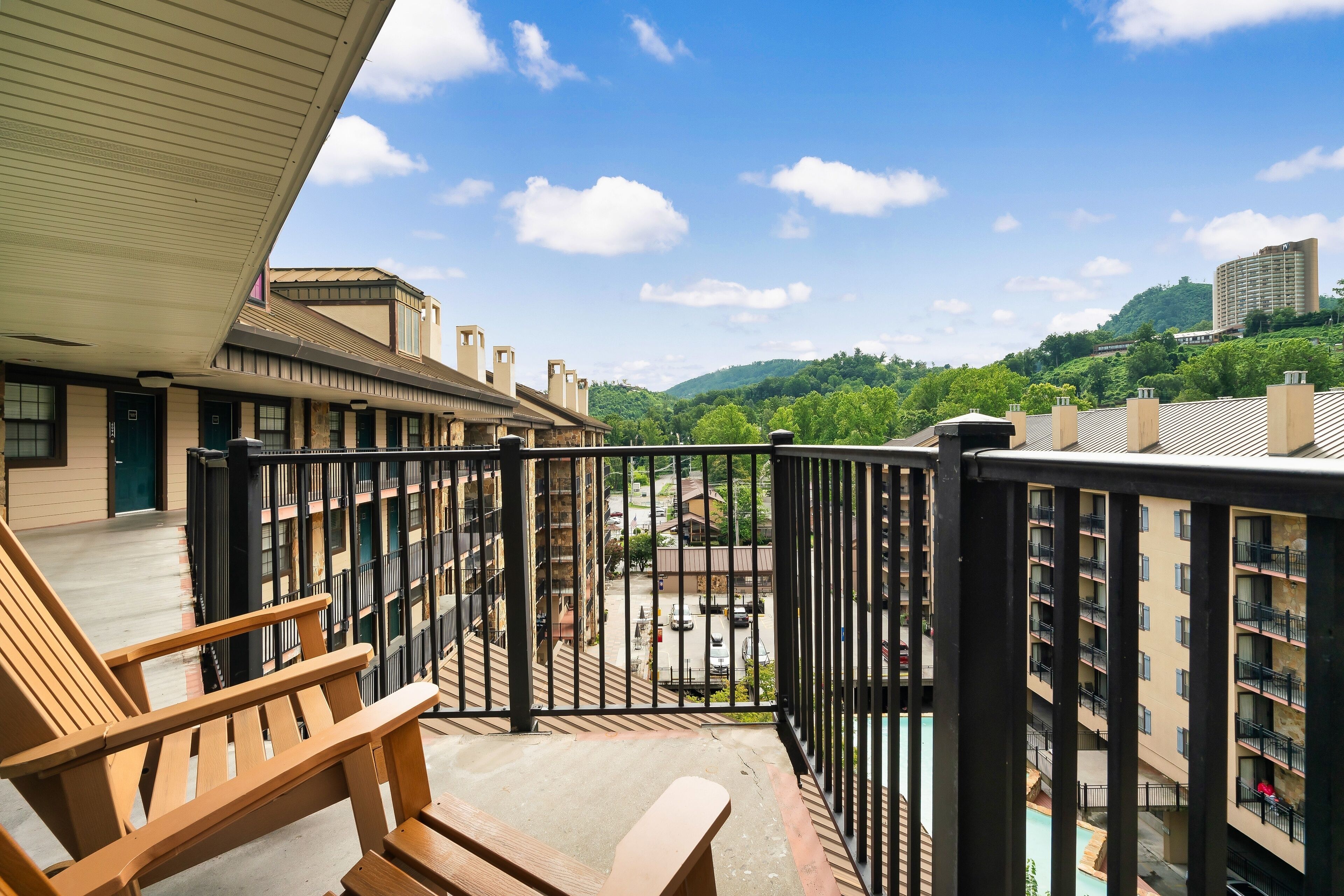 A balcony with a wooden chair, a view of a parking area, and a building with multiple balconies.