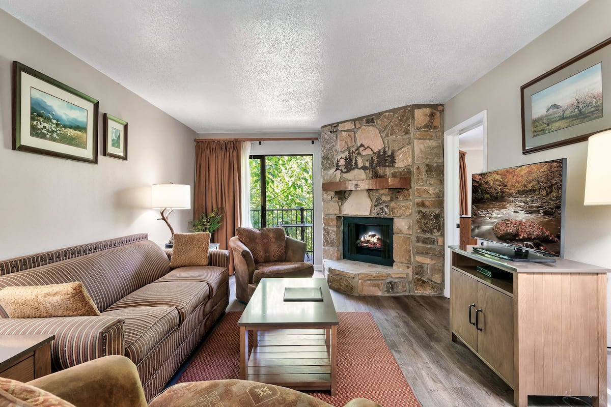 A living room with a stone fireplace, a sofa, a coffee table, and a television.