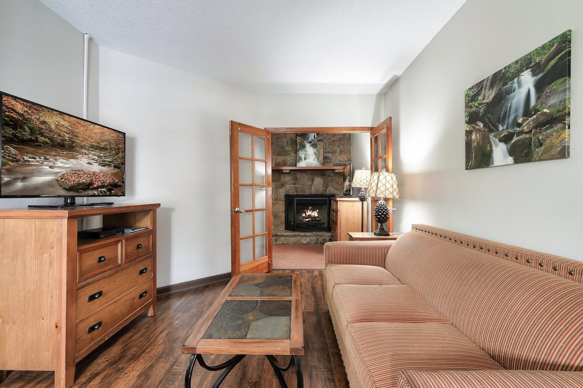 A living room with a wooden cabinet, a stone coffee table, a striped sofa, a fireplace, and a painting of a waterfall.