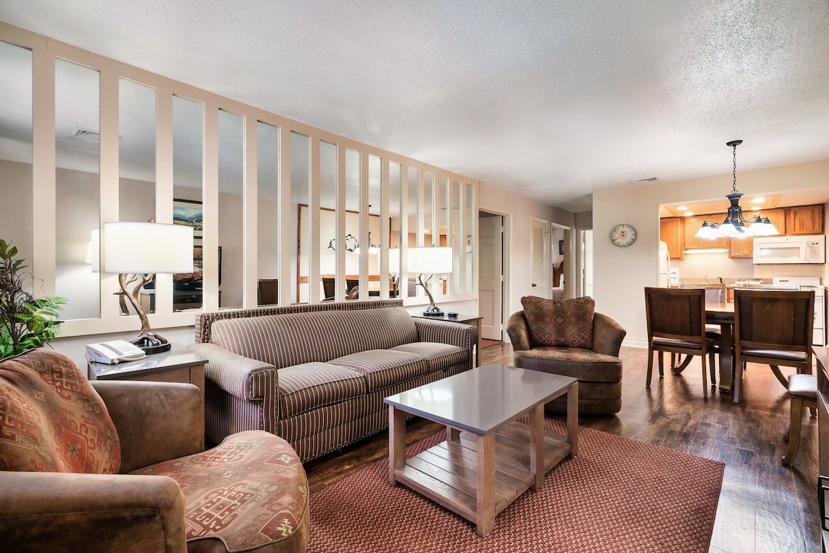 A living room with a sofa, armchairs, a coffee table, and a dining area with chairs and a table.