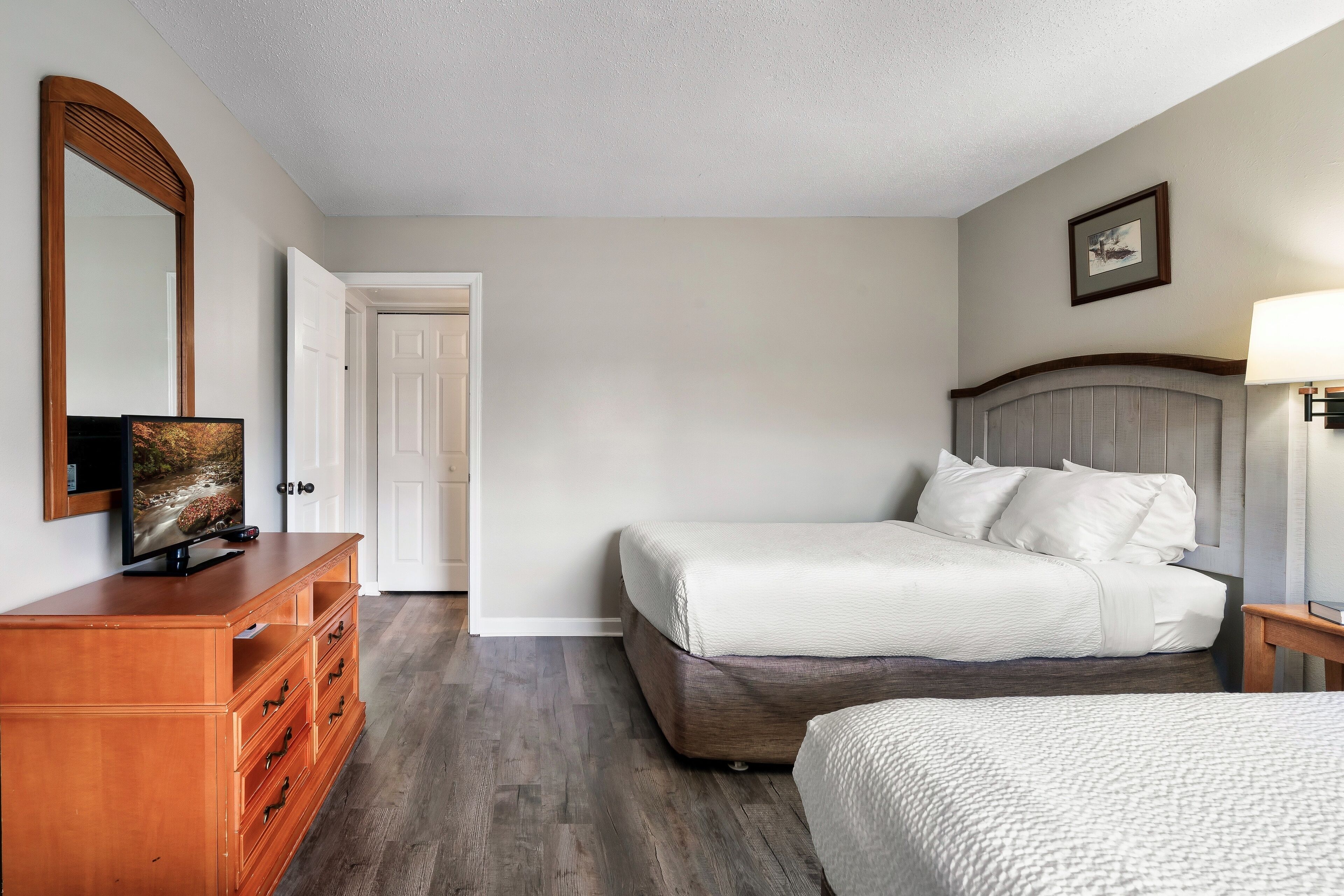 A bedroom with a bed, a dresser, a television on the dresser, and a door.