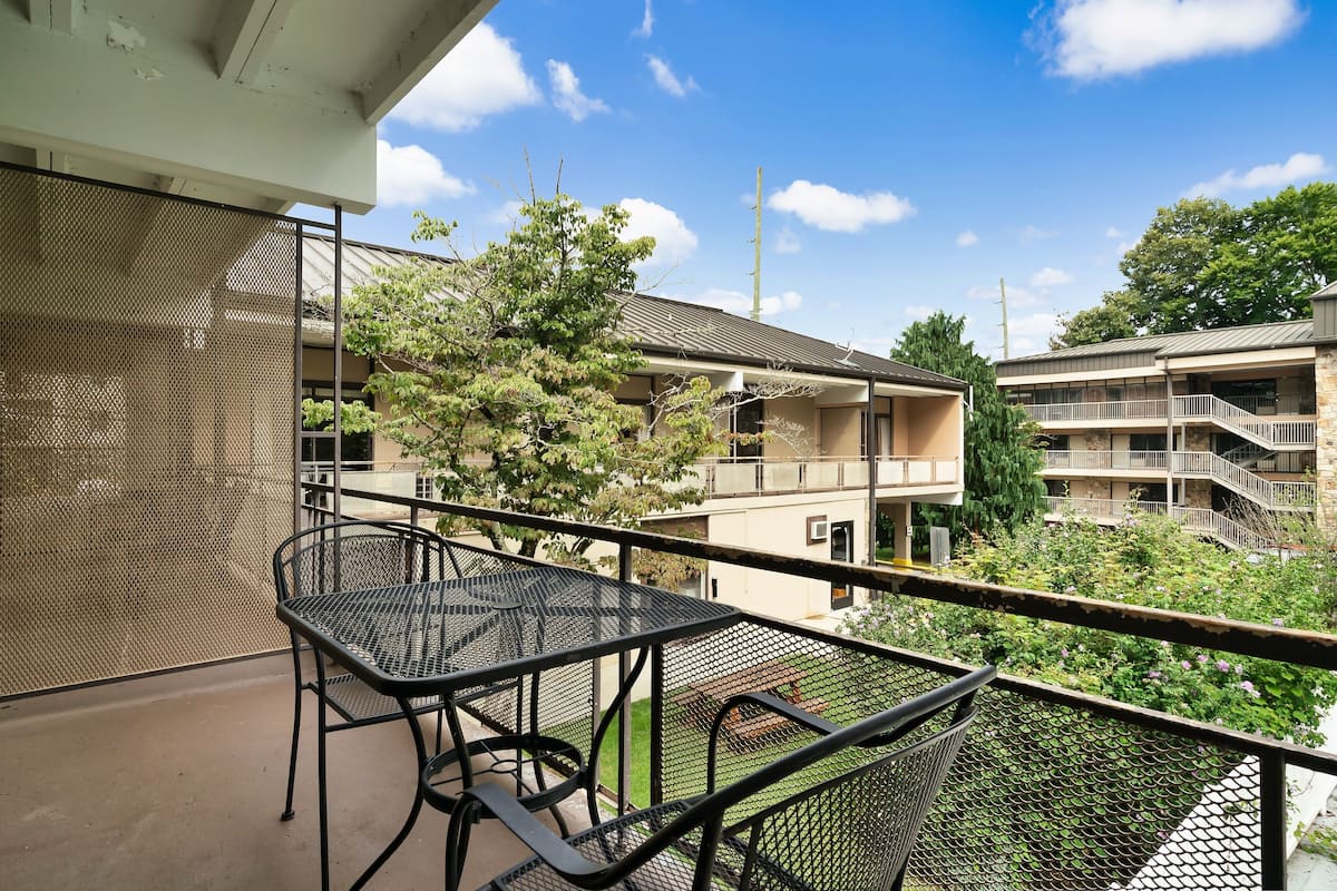 A balcony with a metal table and chairs, overlooking a building with multiple balconies and a garden.