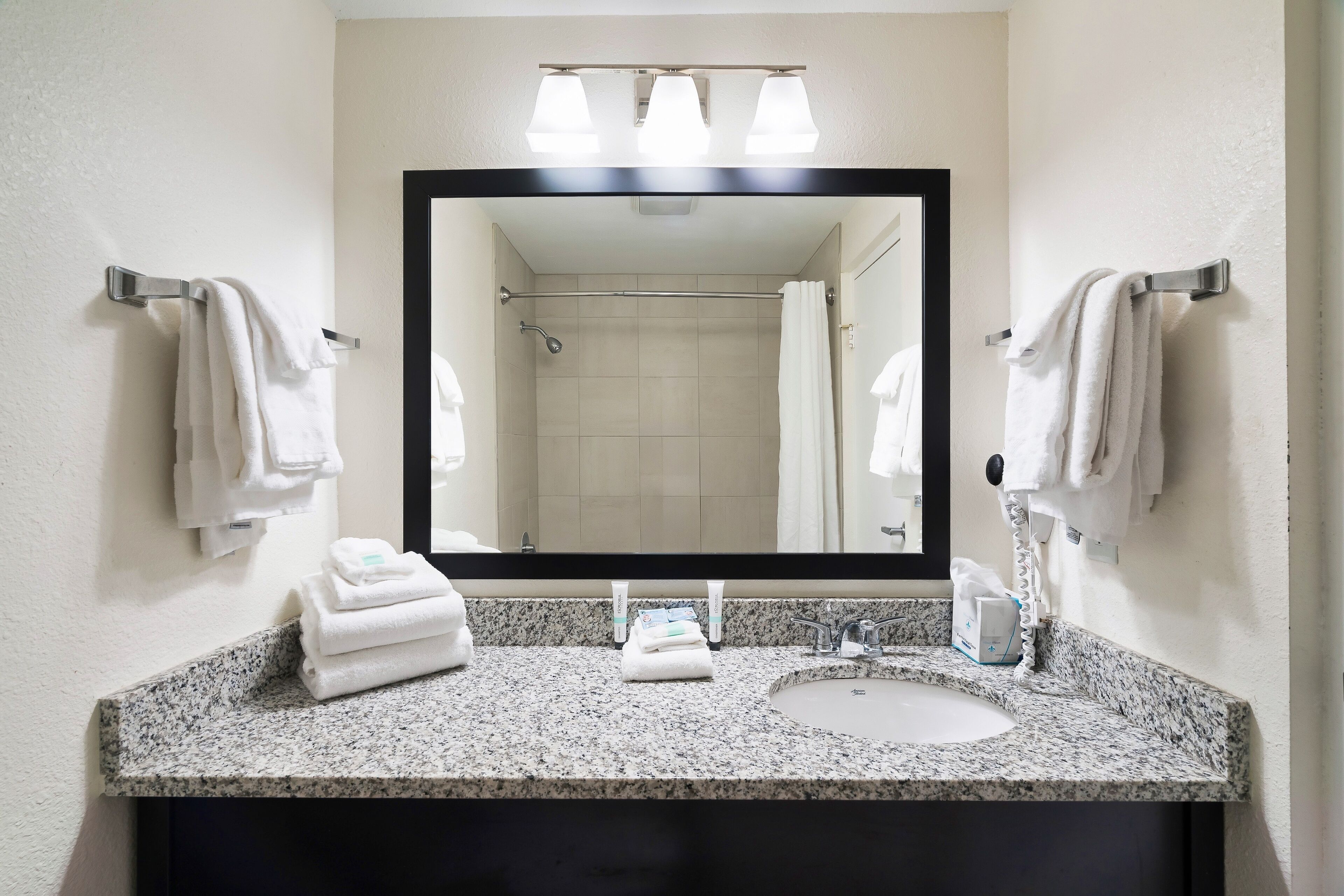 A bathroom with a granite countertop, a sink, a mirror, and two towel racks.