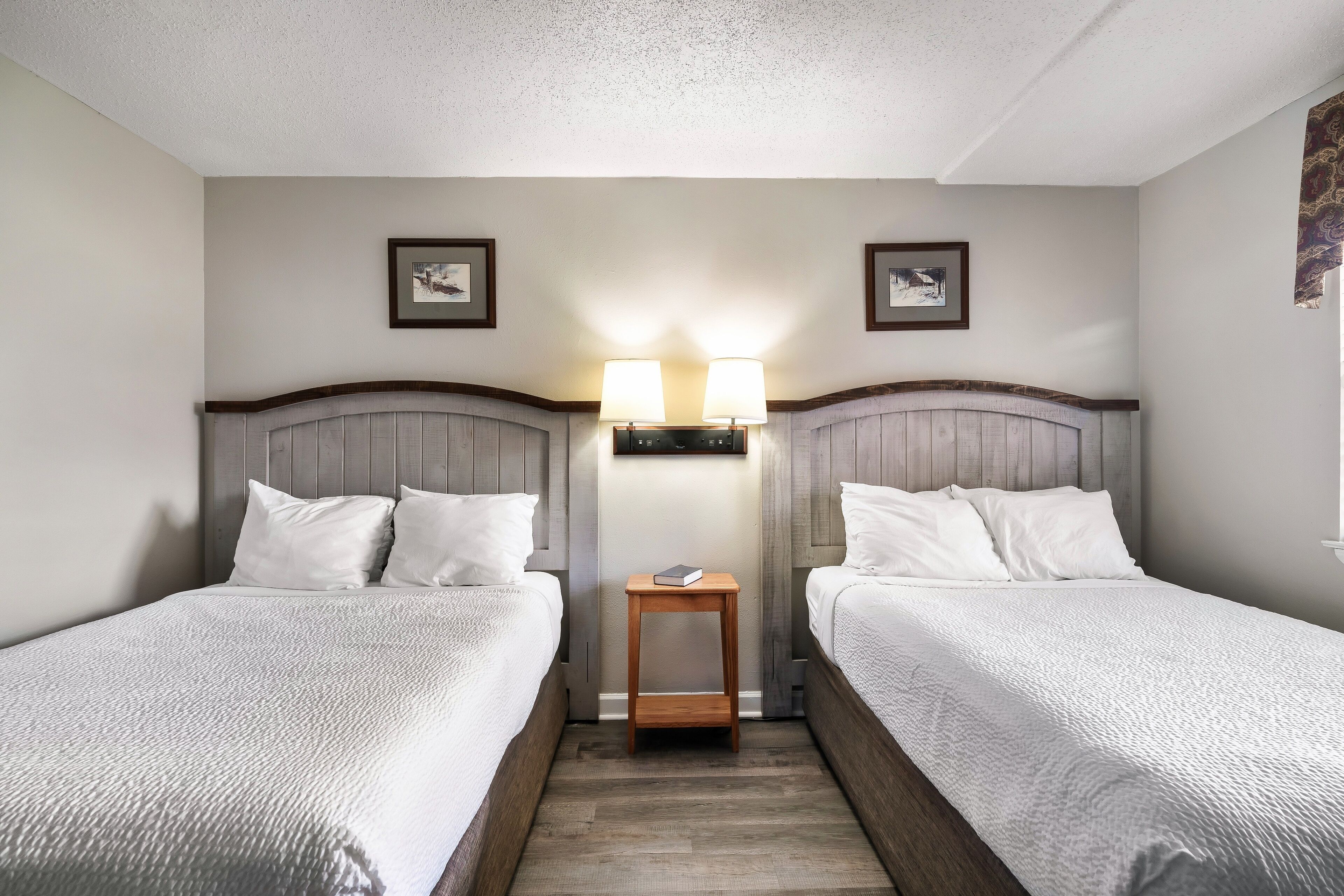 Une chambre d’hôtel avec deux lits, une table de chevet et des lampes fixées au mur.