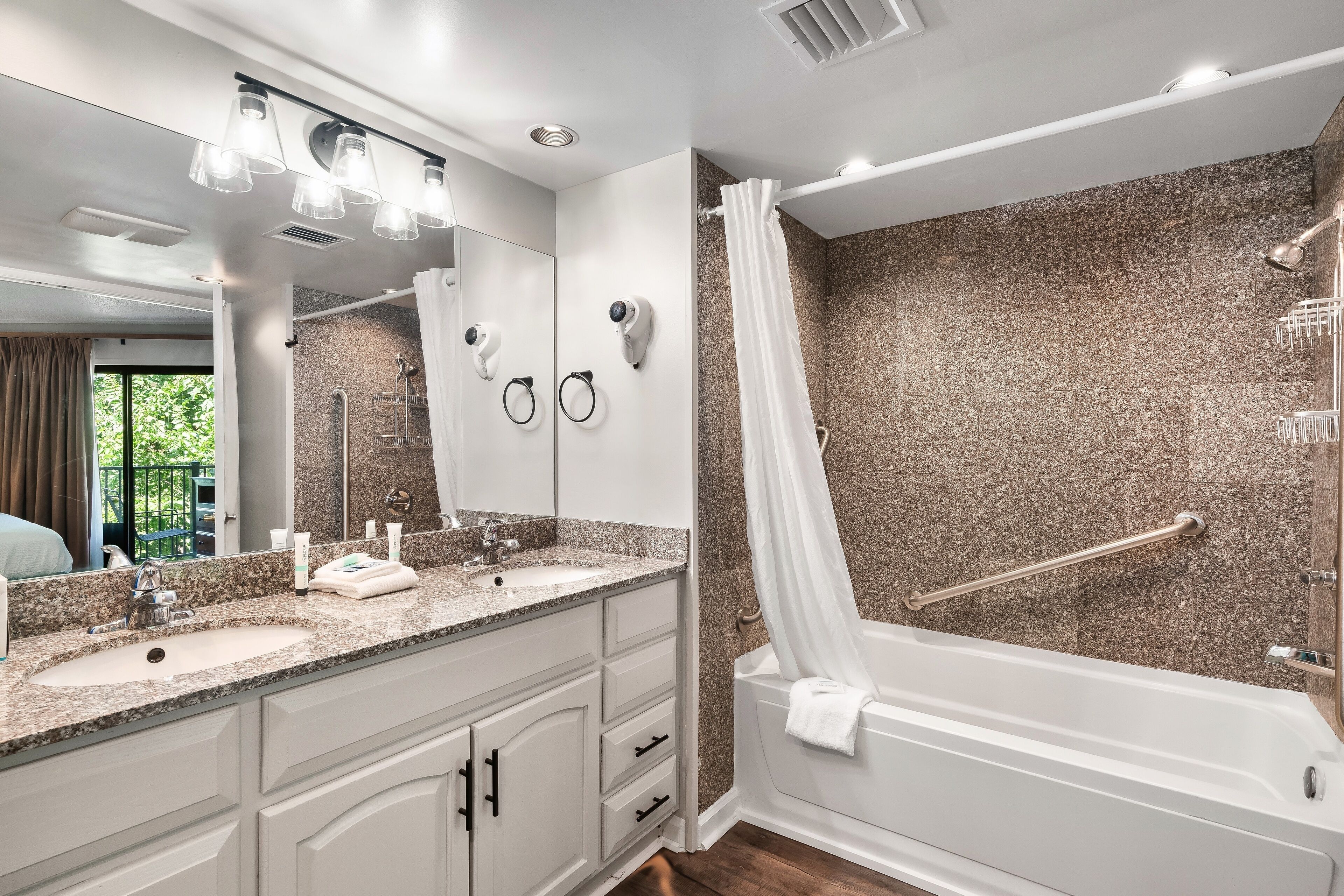 A modern bathroom with a granite countertop sink, a large mirror, and a walk-in shower with a glass door.