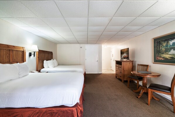 A hotel room with two beds, a desk, a chair, a lamp, and a painting on the wall.