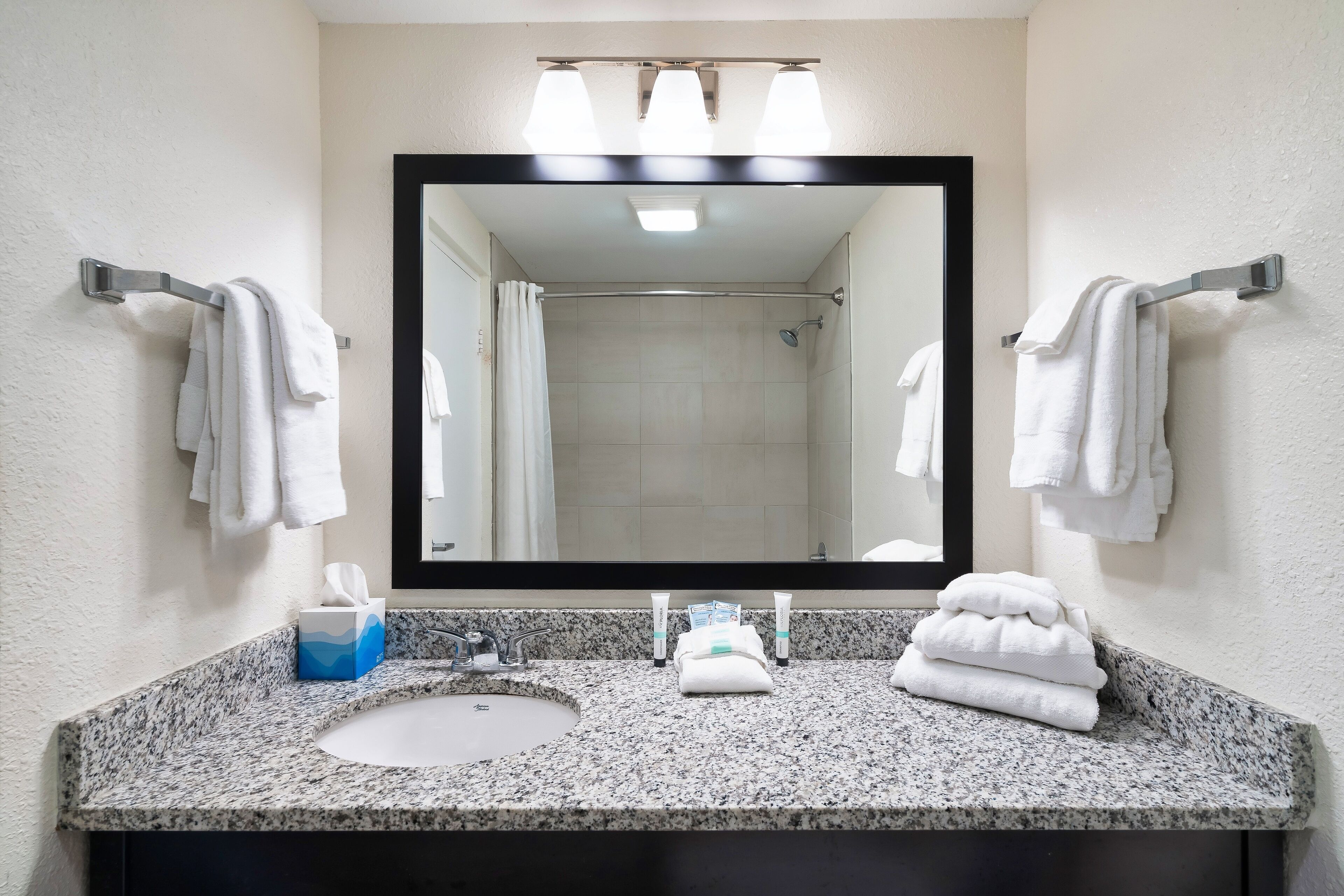 Une salle de bain avec un grand miroir, deux porte-serviettes, un lavabo et une douche.