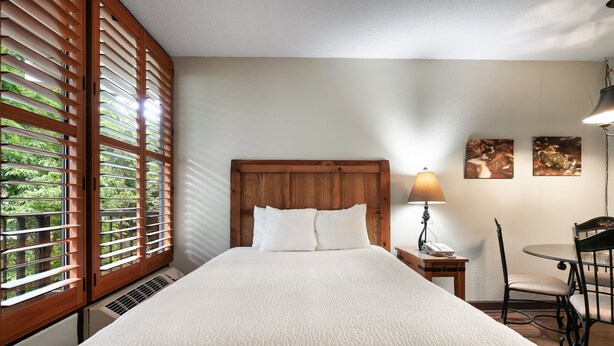 Una cama bien hecha con cabecera de madera, una mesita de noche con lámpara y dos cuadros enmarcados en la pared.