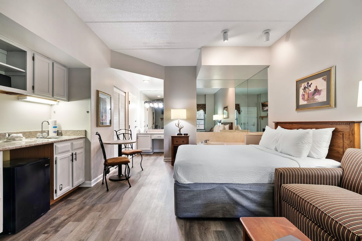 A hotel room with a bed, a small sofa, a desk with a chair, a kitchenette, and a bathroom.