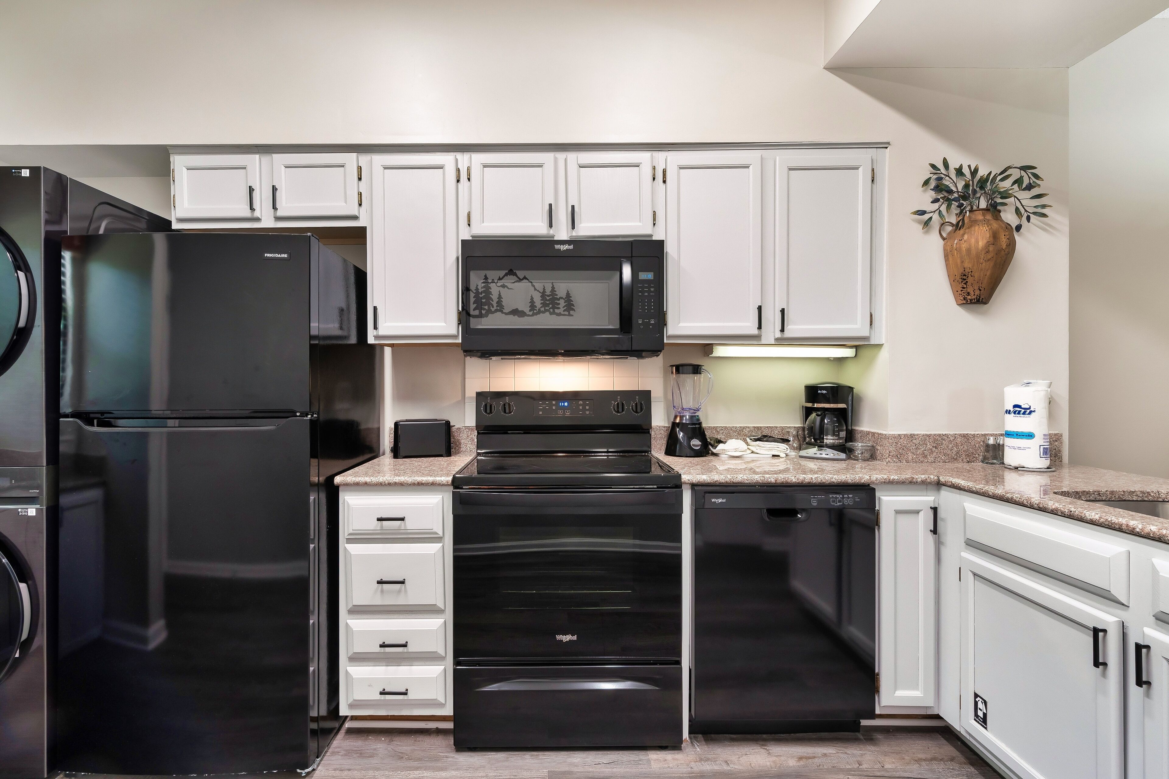 Una cocina moderna con armarios blancos, un refrigerador negro, un microondas, un horno y un lavavajillas.