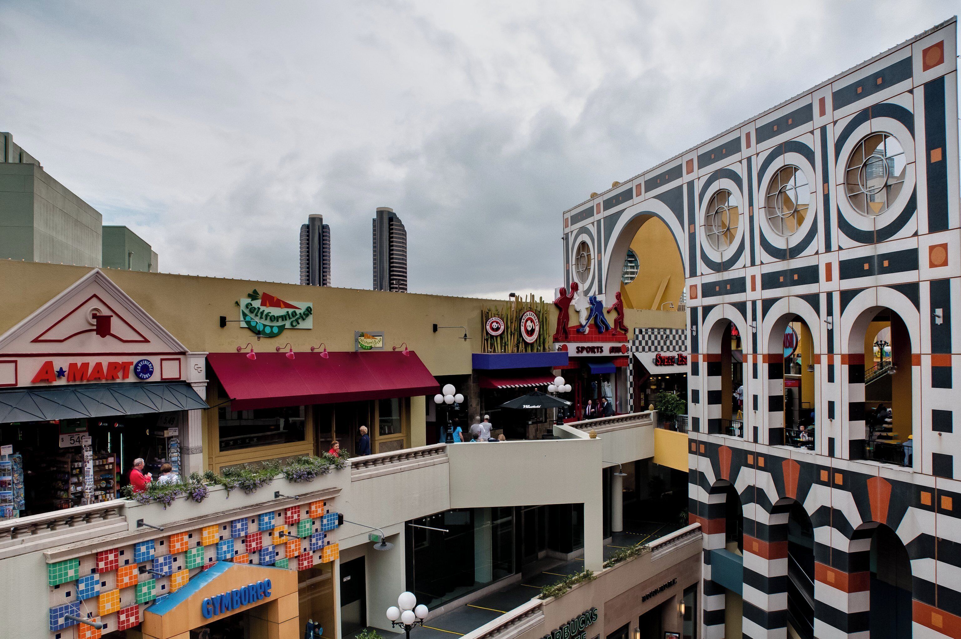Un centro comercial de varios niveles con diversas tiendas, incluyendo un gimnasio, y un diseño arquitectónico distintivo con ventanas circulares y un patrón de cuadros en el nivel superior.