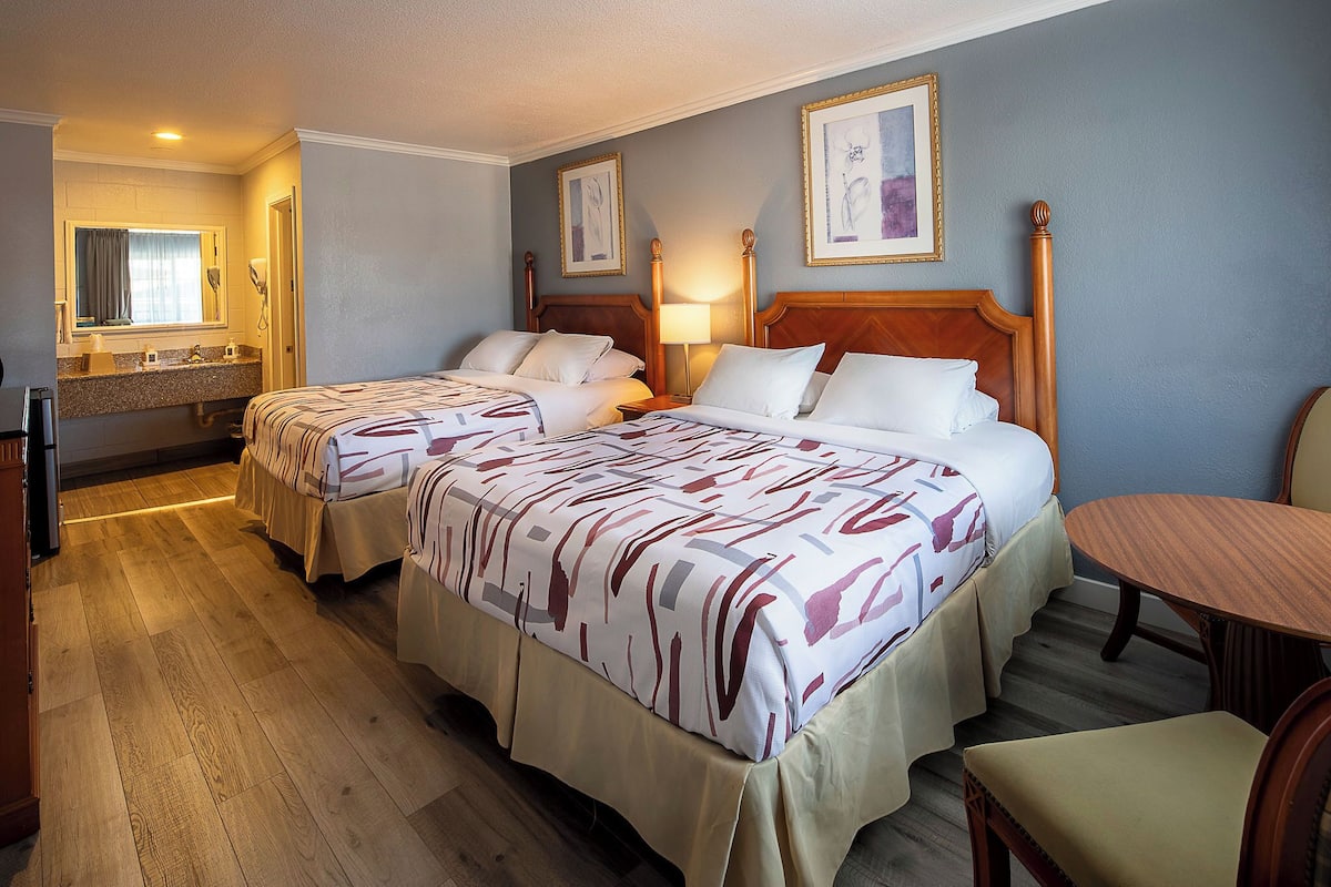Quarto de hotel com duas camas, banheiro e uma pequena mesa de jantar.