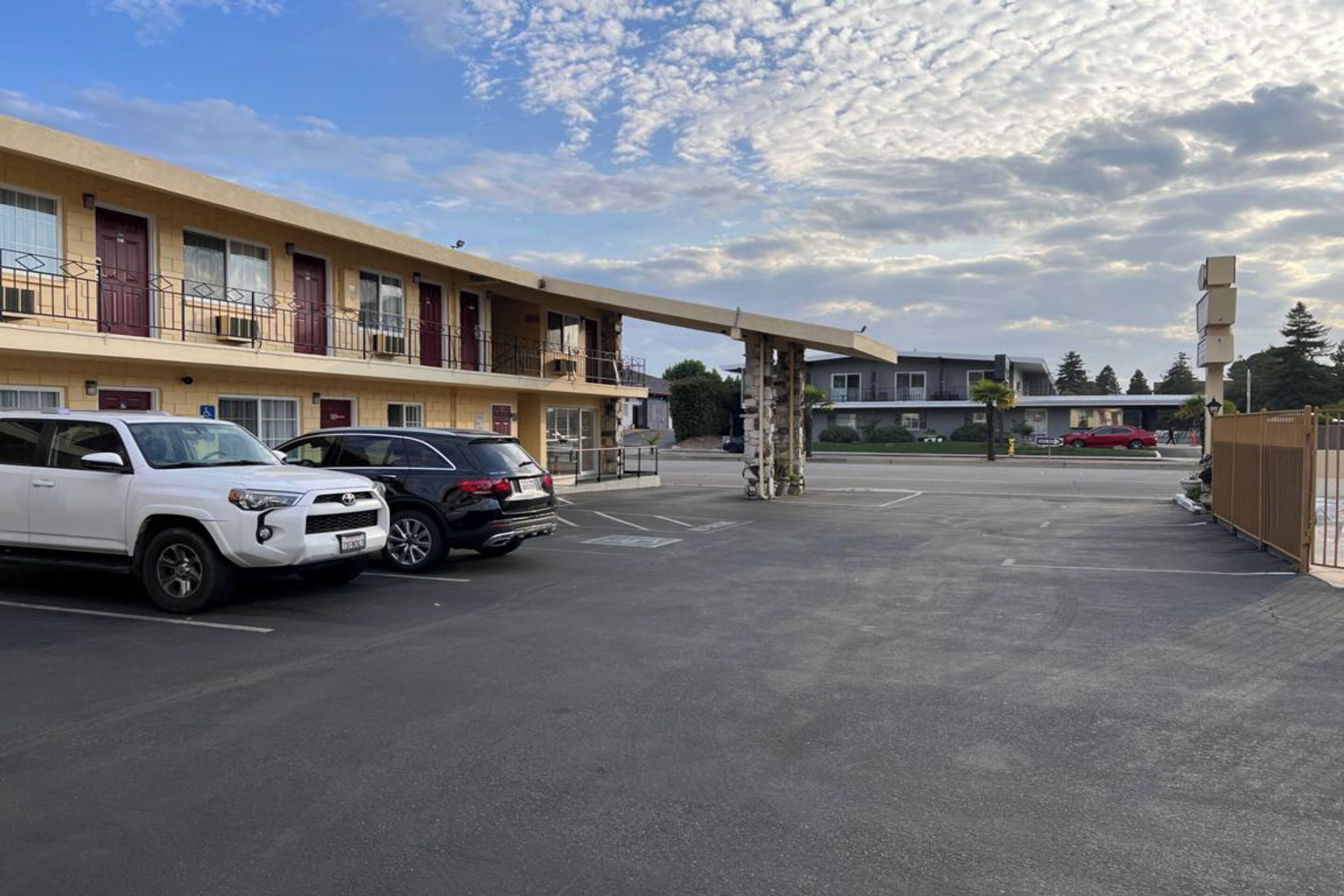 A multi-story motel with a parking lot, a covered walkway, and a clear sky.