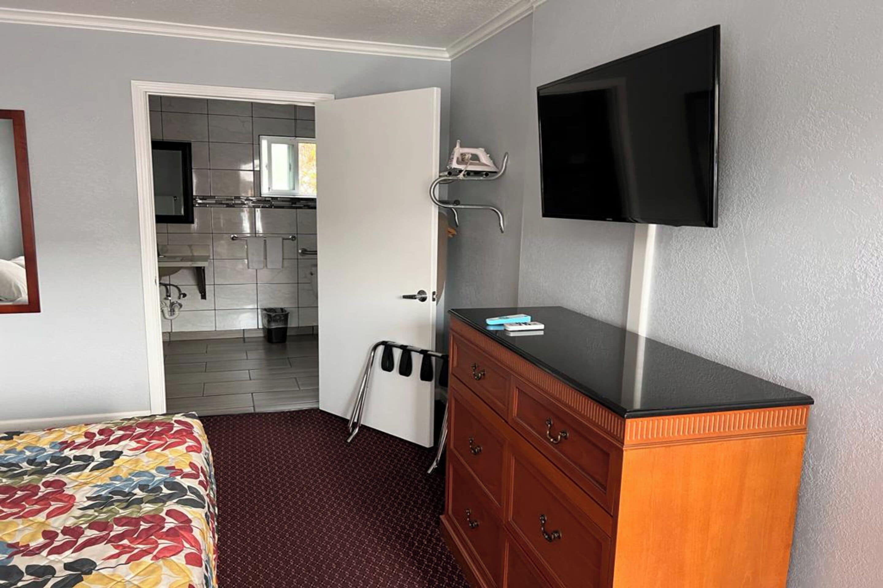 Habitación de hotel con una cama, un aparador de madera, un televisor y una kitchenette al fondo.