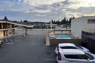 Un estacionamiento con piscina, un coche blanco y un edificio con balcón.