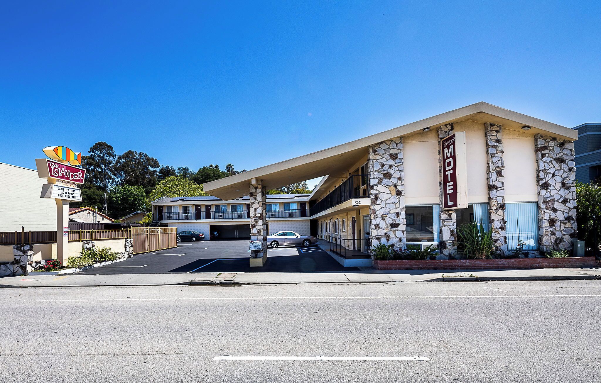 Un motel avec une façade en pierre, un panneau indicateur et un parking.