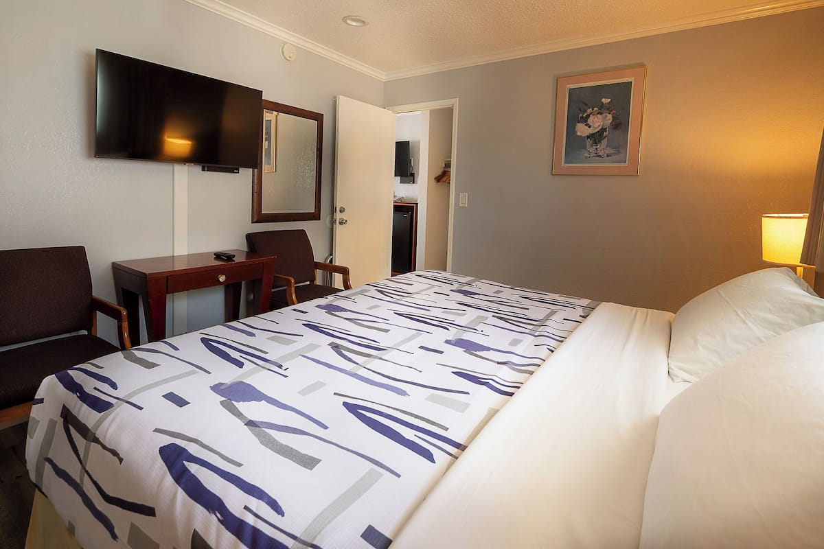 Quarto de hotel com cama, secretária, cadeira, televisão e porta para um banheiro.