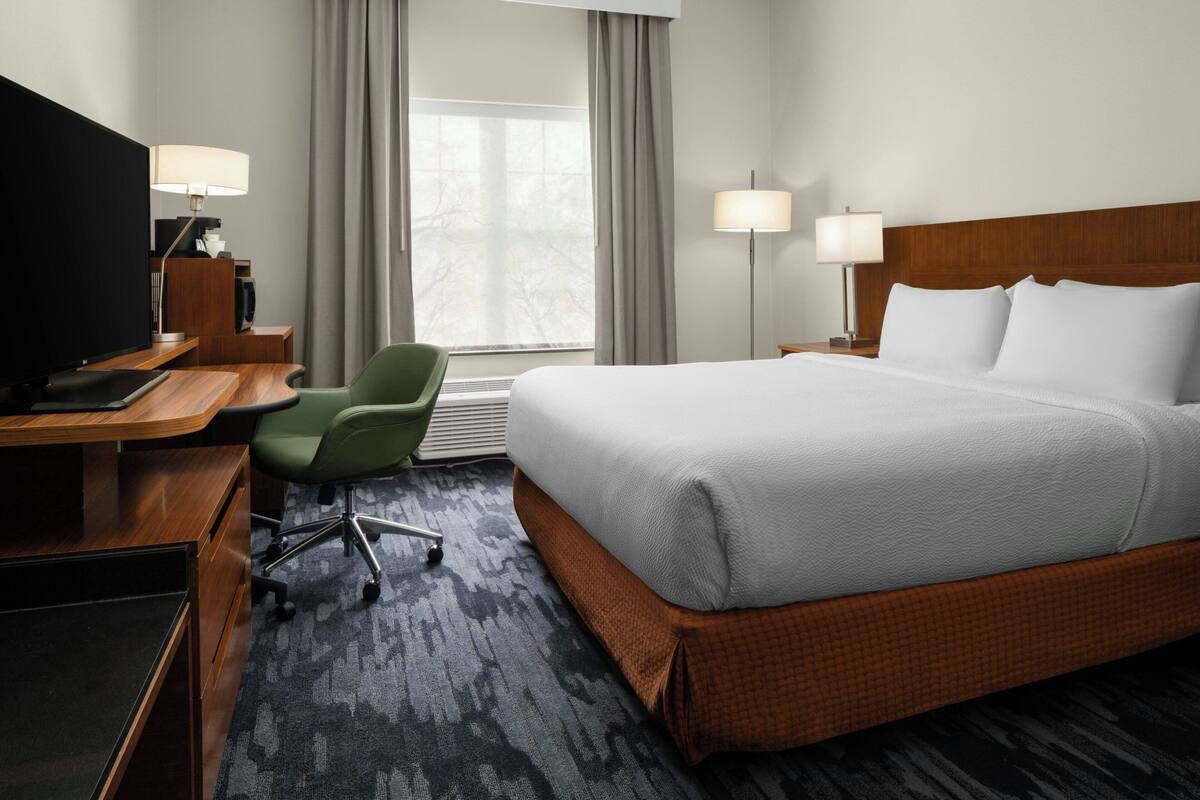 A hotel room with a bed, desk, chair, TV, and two lamps.