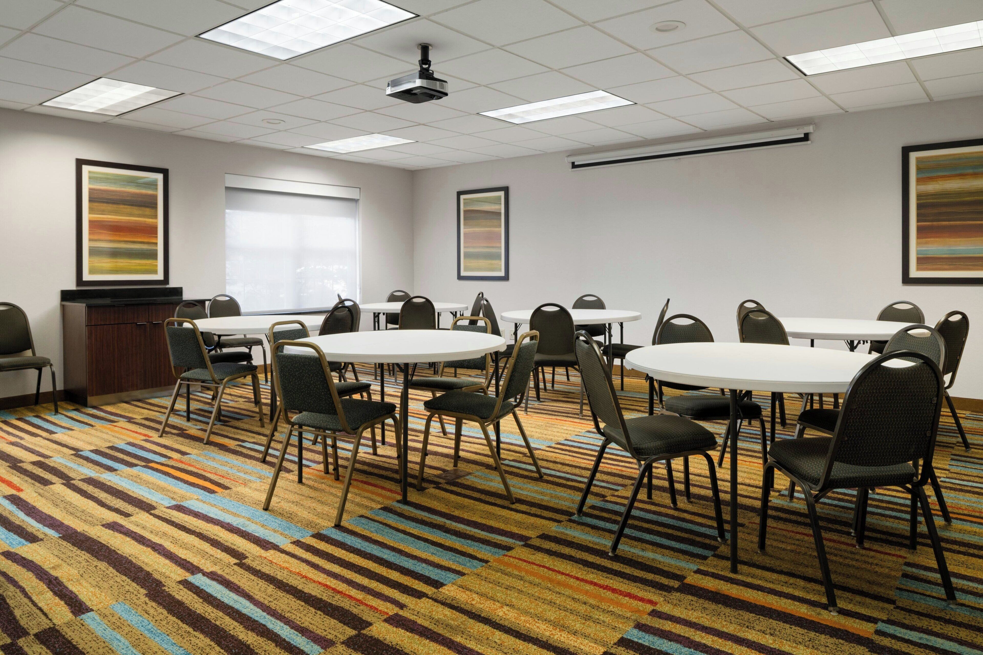 A conference room with multiple tables and chairs, a projector, and a patterned carpet.