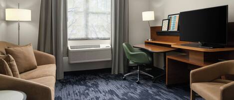 A hotel room with a sofa, a desk with a computer, a television, and a window with curtains.