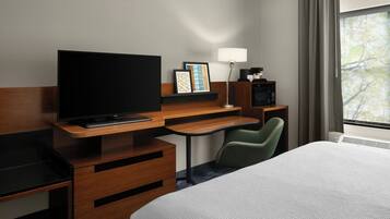 A hotel room with a bed, a desk with a TV, a chair, a lamp, and a microwave.