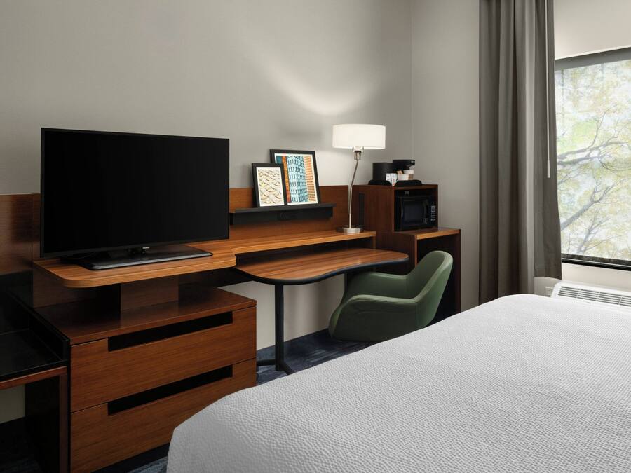 A hotel room with a bed, a desk with a TV, a chair, a lamp, and a microwave.