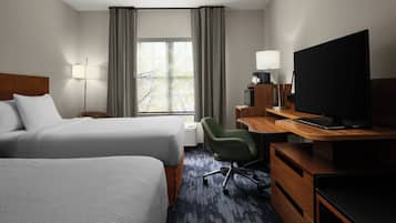 Habitación de hotel con dos camas, un escritorio con computadora, televisor y ventana con cortinas.