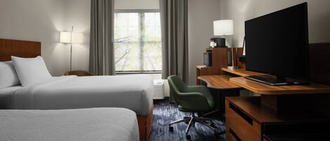 A hotel room with two beds, a desk with a computer, a television, and a window with curtains.