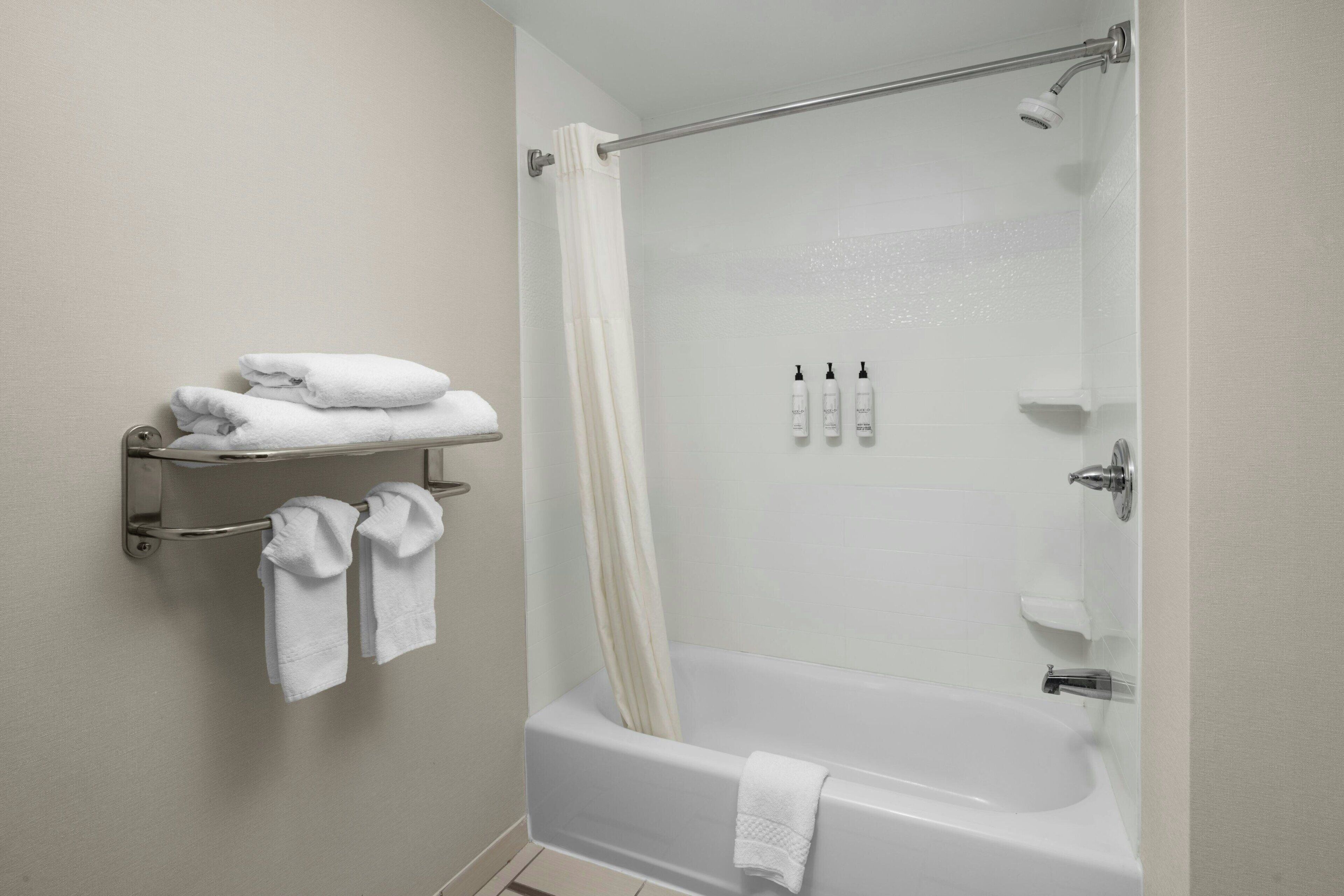 A modern bathroom with a bathtub, a shower curtain, and a towel rack with folded towels.