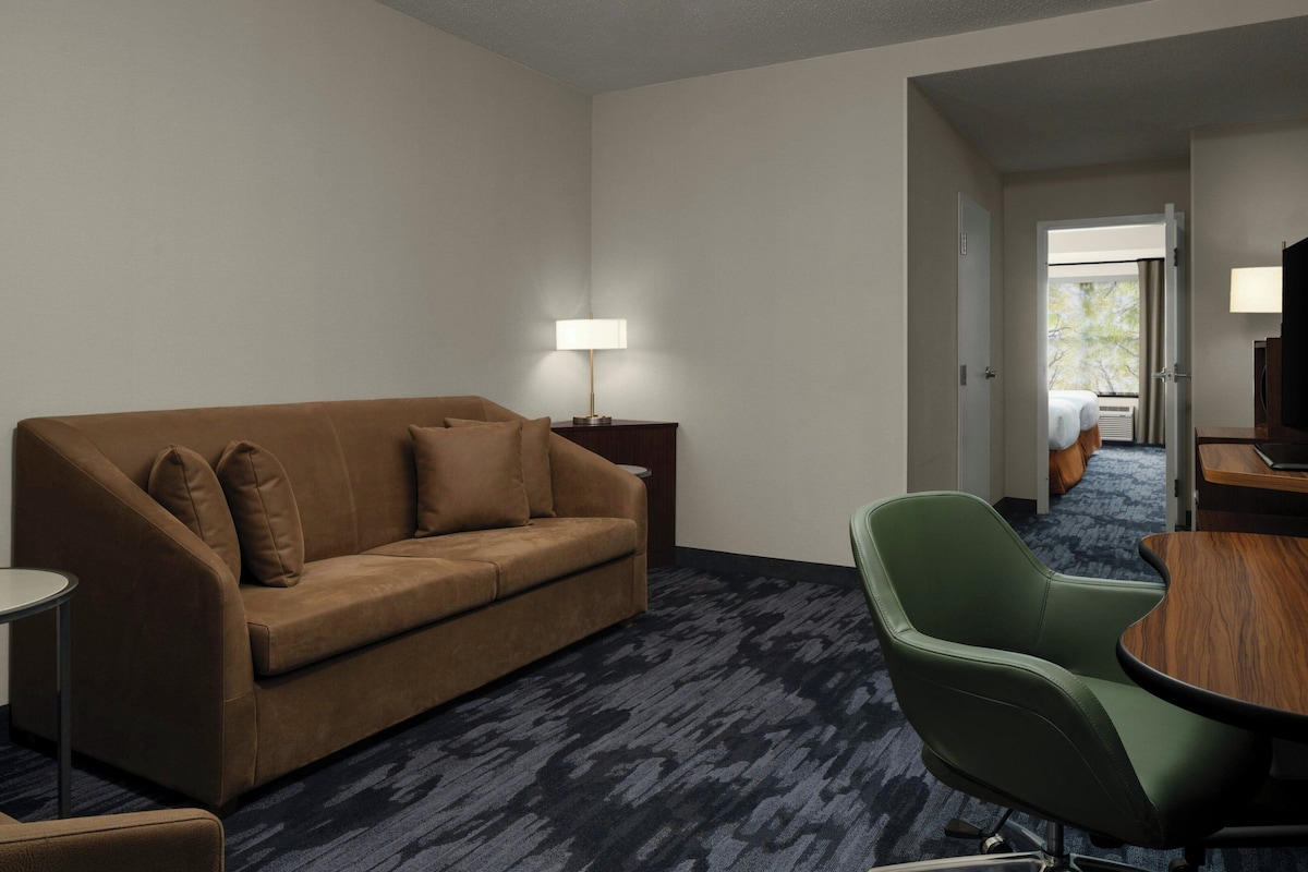 Ein Hotelzimmer mit einem braunen Sofa, einem grünen Sessel, einem kleinen Tisch und einer Lampe.