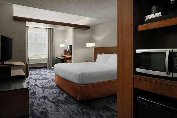 A hotel room with a bed, a desk, a television, a microwave, and a window with curtains.