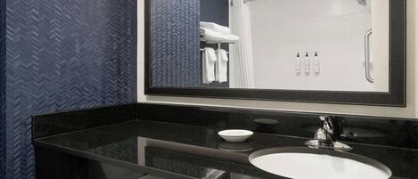 Un baño moderno con encimera negra, lavamanos blanco y un espejo grande.
