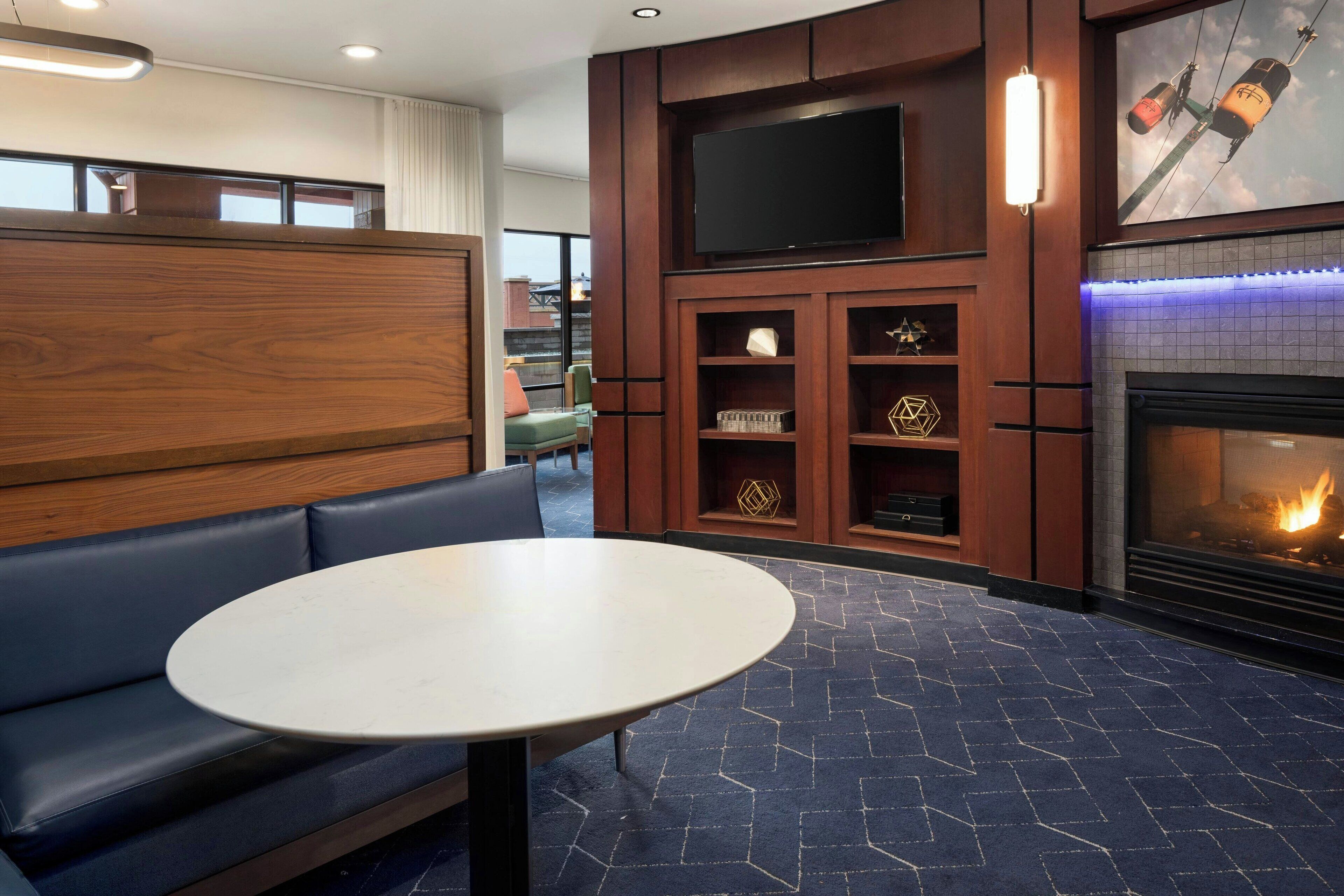 A modern lounge area with a sofa, a round table, a fireplace, and a mounted TV.