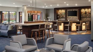 A modern bar area with a long counter, multiple bar stools, and a television mounted on the wall.
