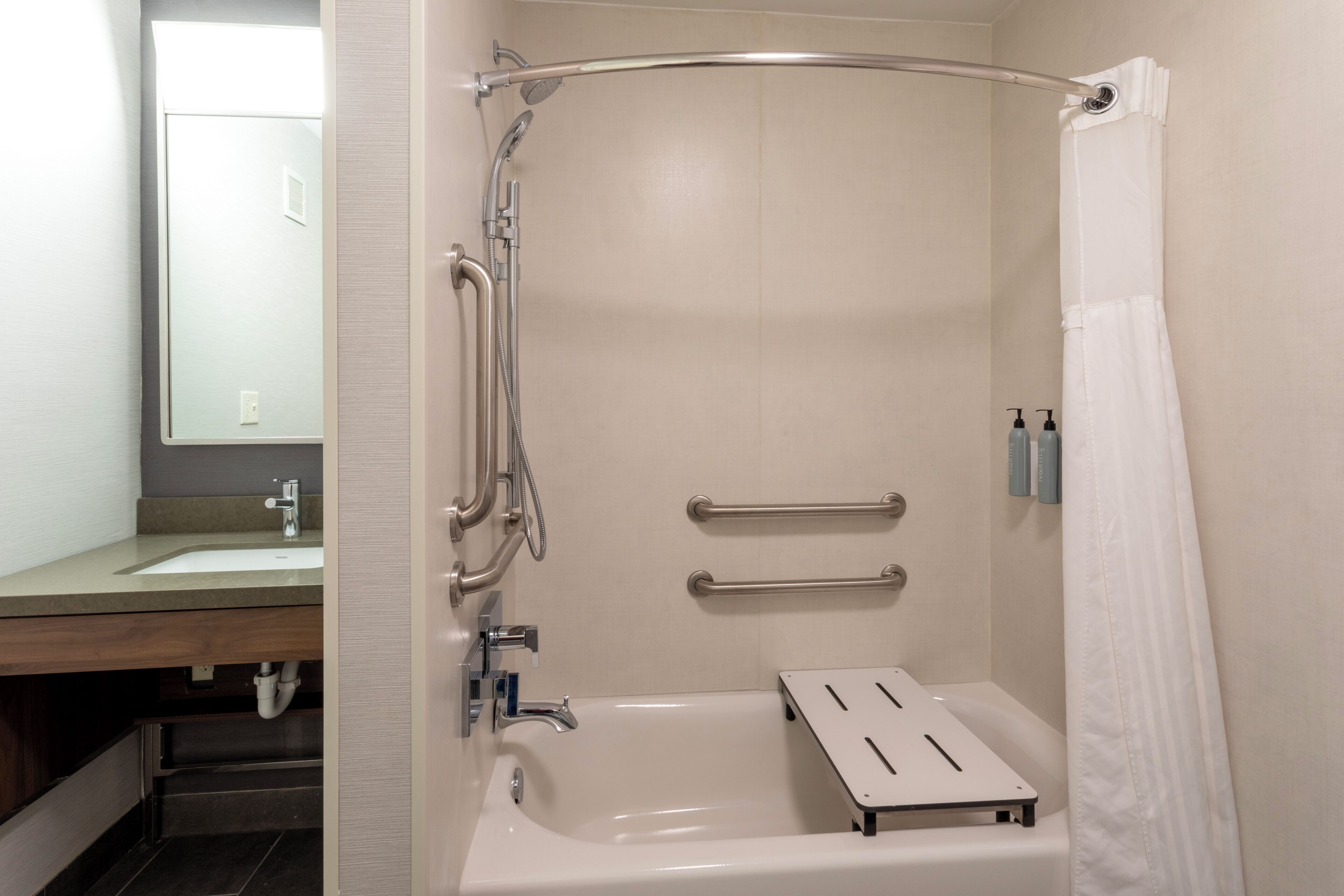 A bathroom with a bathtub, a shower, and a toilet. There are grab bars installed for safety.