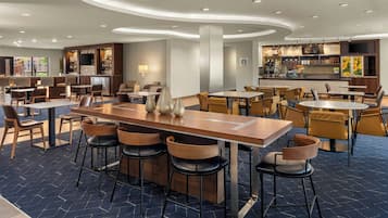 Un restaurante moderno con barra central, varias zonas de estar y cocina al fondo.