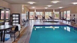 A swimming pool area with lounge chairs, a table, and a tiled floor.