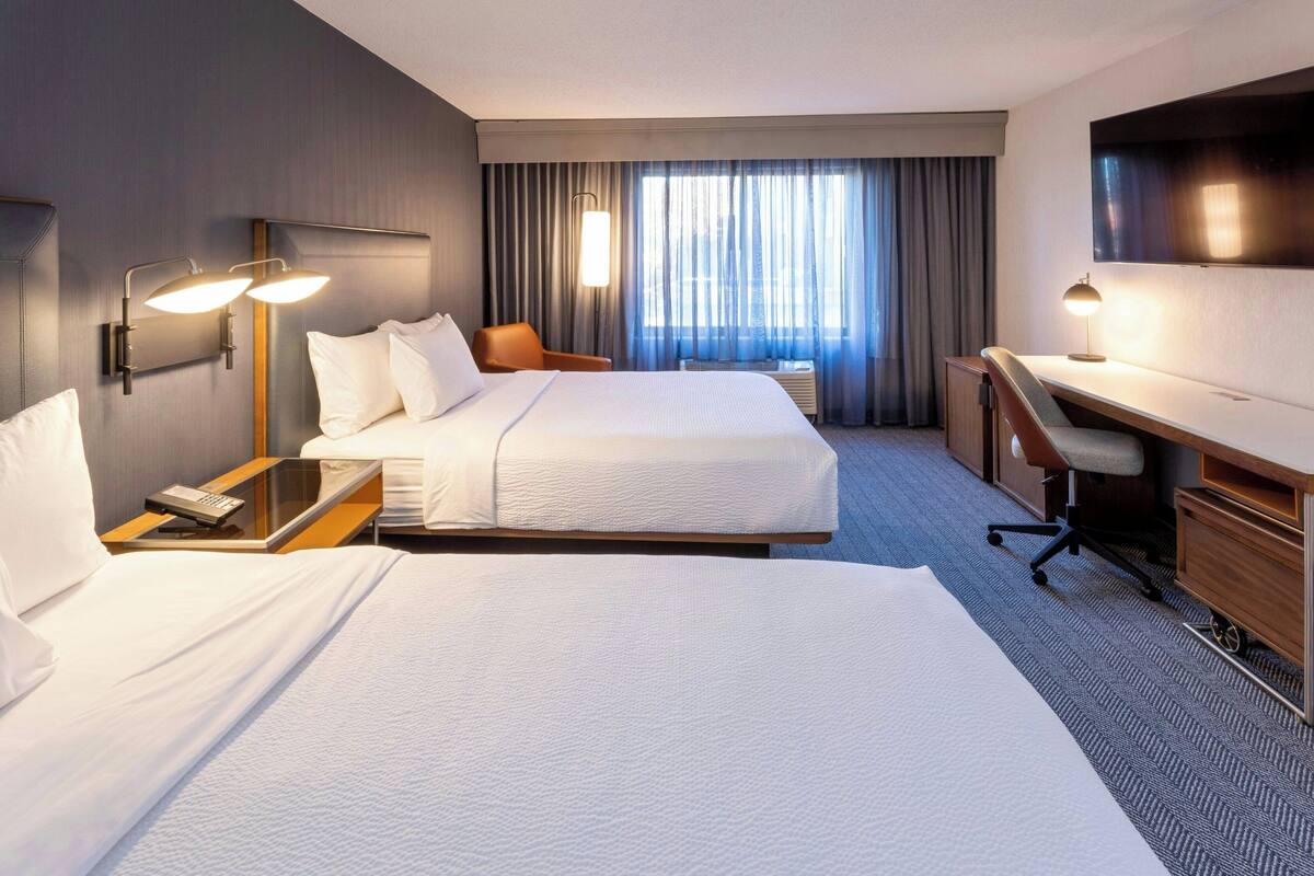 Een hotelkamer met twee bedden, een bureau, een stoel, een televisie en een raam met gordijnen.