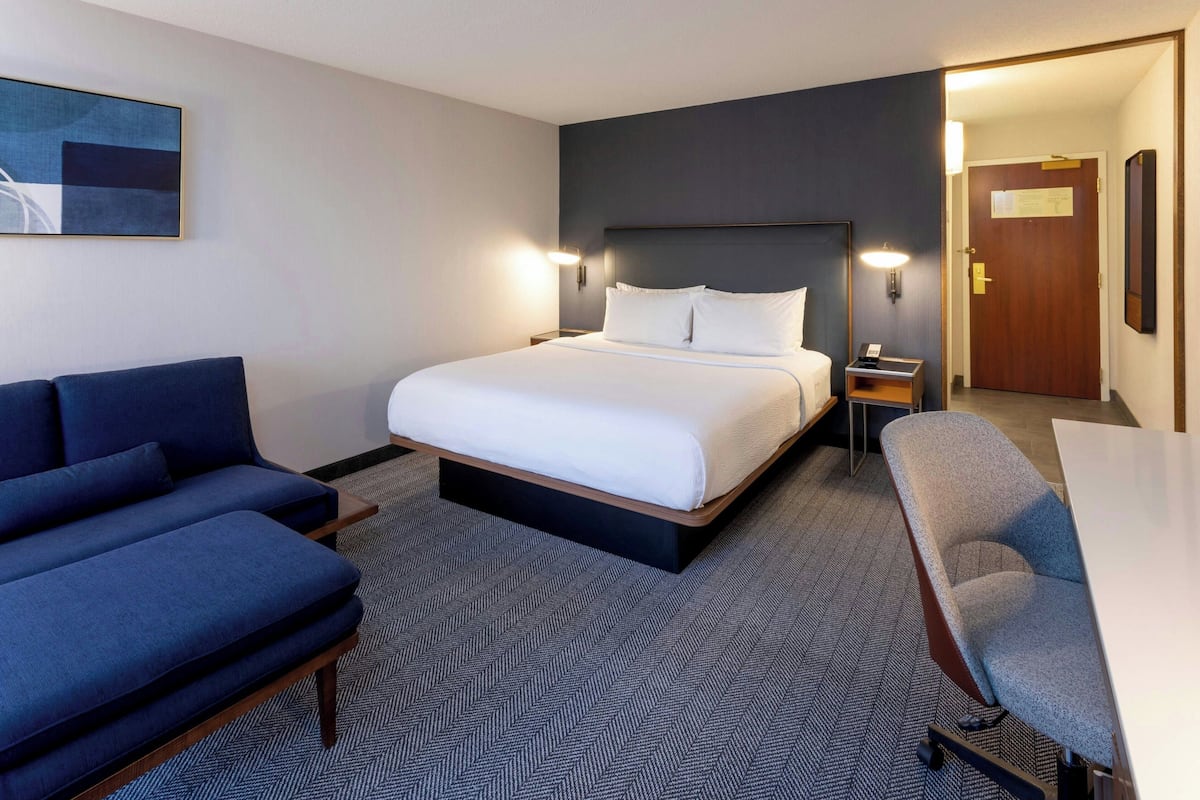 A hotel room with a bed, a sofa, a chair, a desk, and a door.