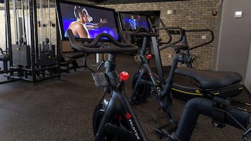 A gym with stationary bikes, a television displaying a fitness program, and exercise equipment.
