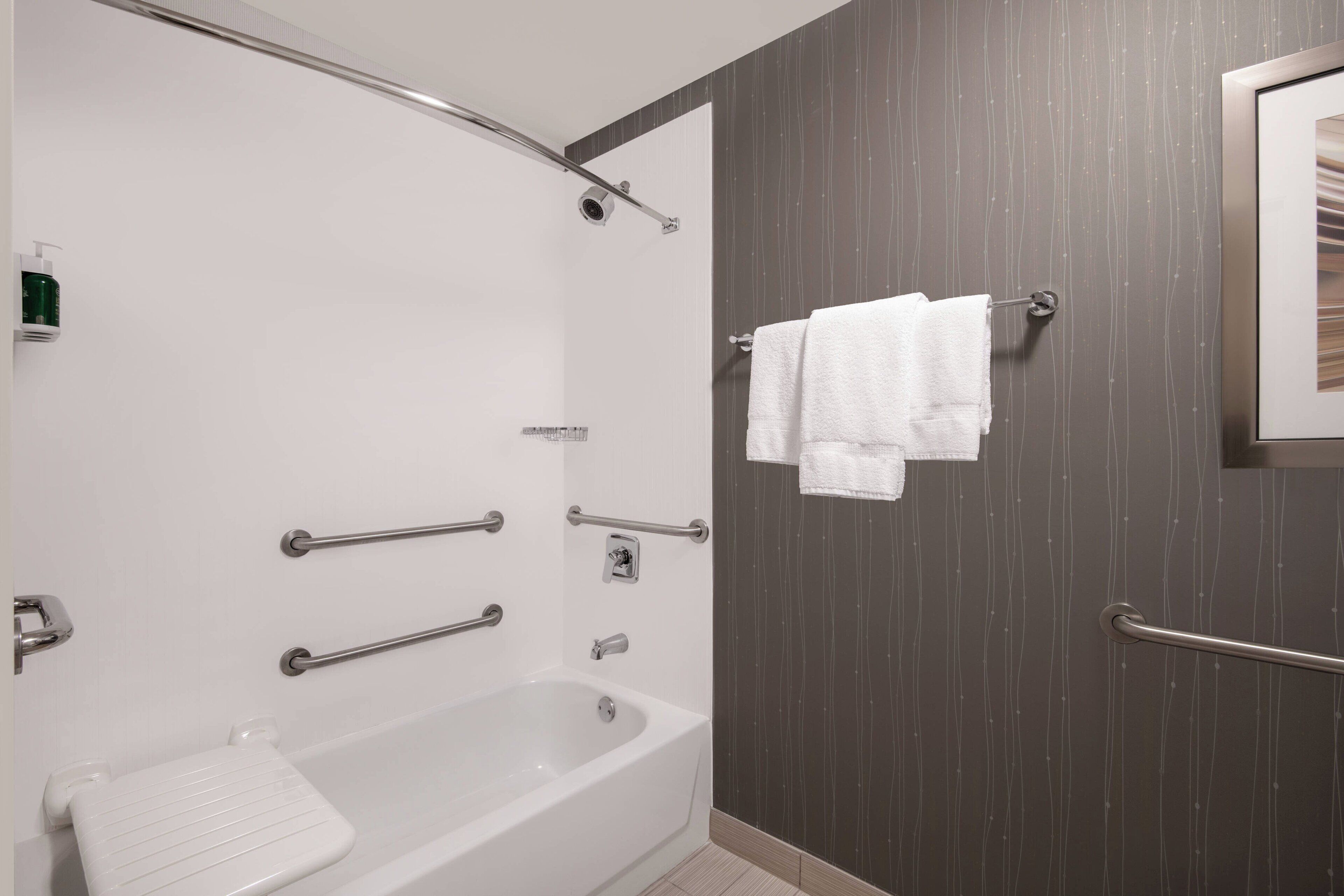 Un baño moderno con bañera, barras de apoyo y un perchero para toallas.