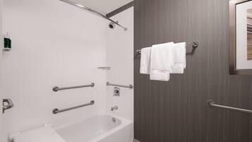 Un baño moderno con bañera, barras de apoyo y un perchero para toallas.