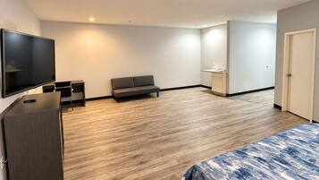 Ein modernes Hotelzimmer mit Flachbildfernseher, einer Sitzecke, einer kleinen Küchenzeile und einem Bett mit einem gemusterten Überwurf.